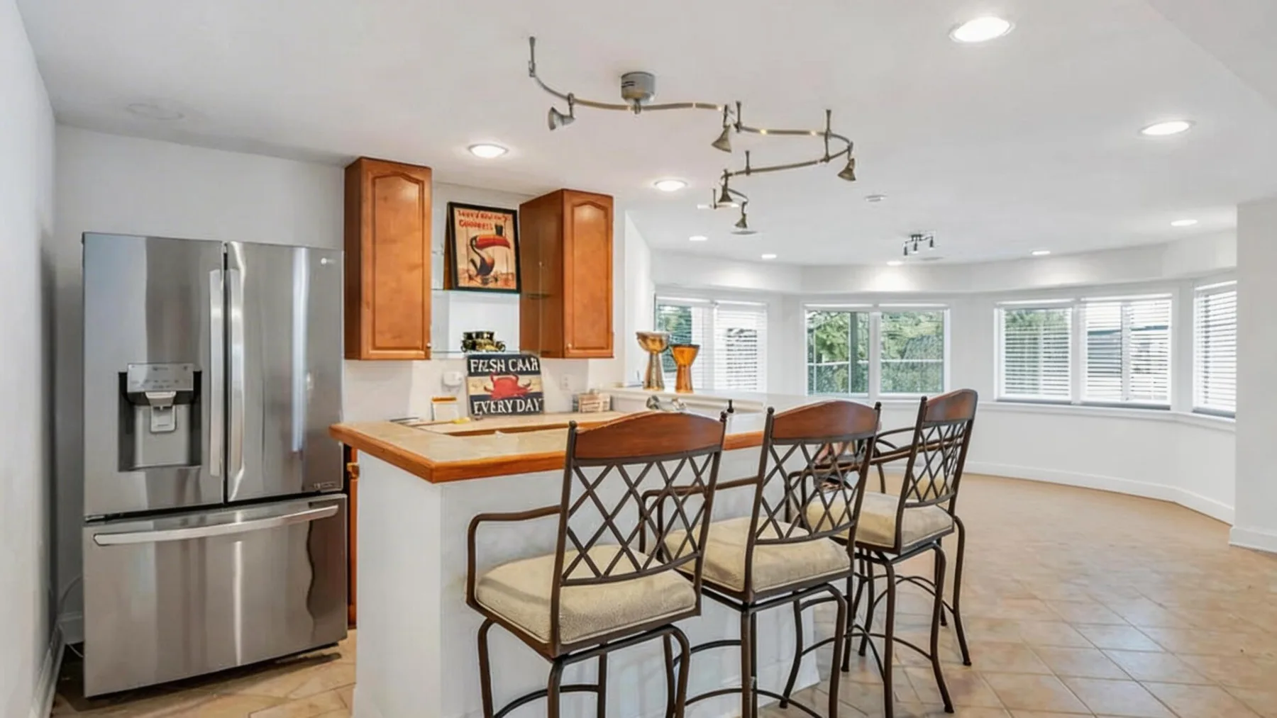 A bright kitchen and dining area with a counter, stools, and stainless steel refrigerator.