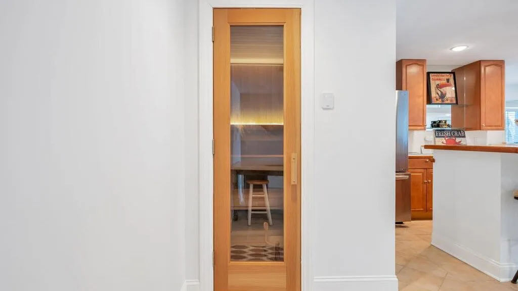 A bright interior hallway opens onto a kitchen, with a narrow glass-paneled door.