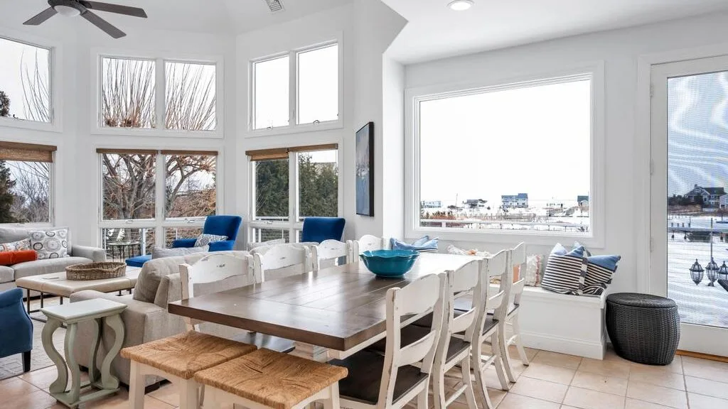 A bright dining area with a long table beside large windows.