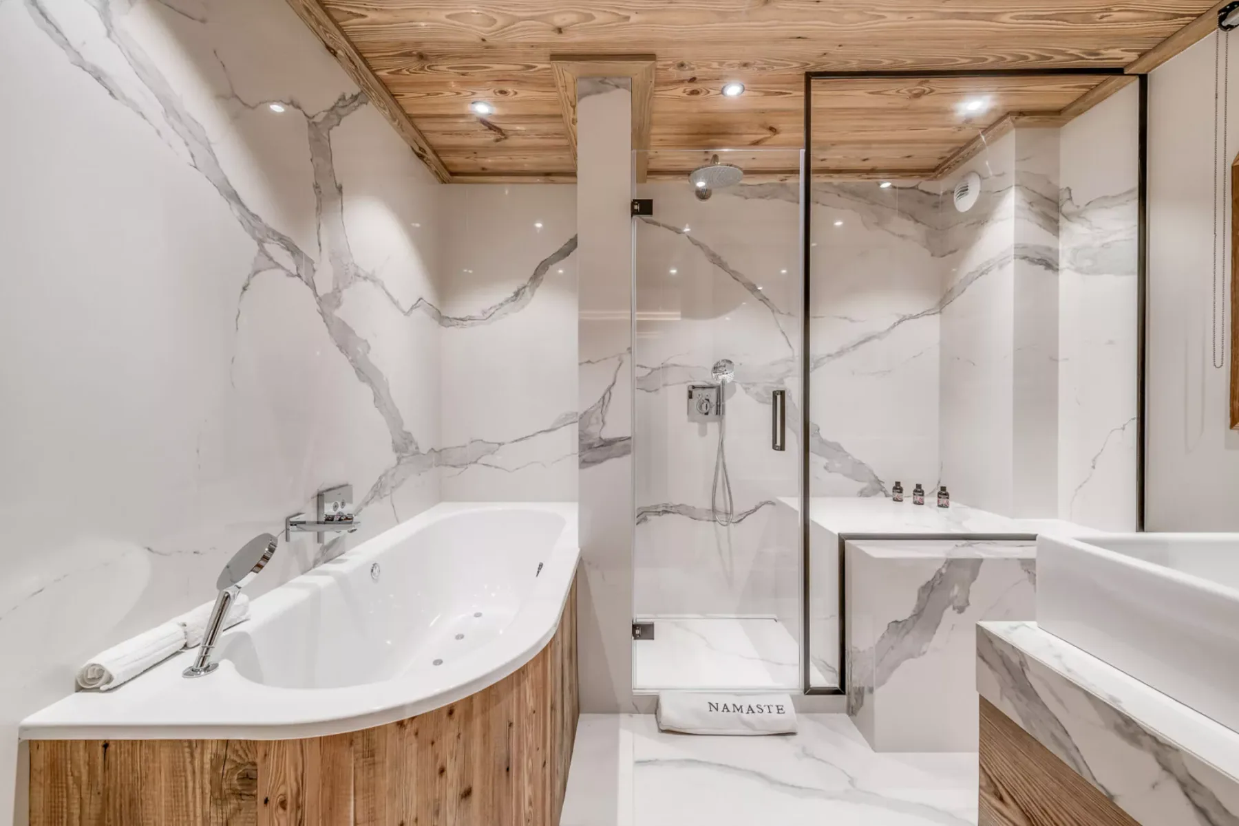 Un baño de mármol con bañera, ducha de vidrio y techo revestido de madera.