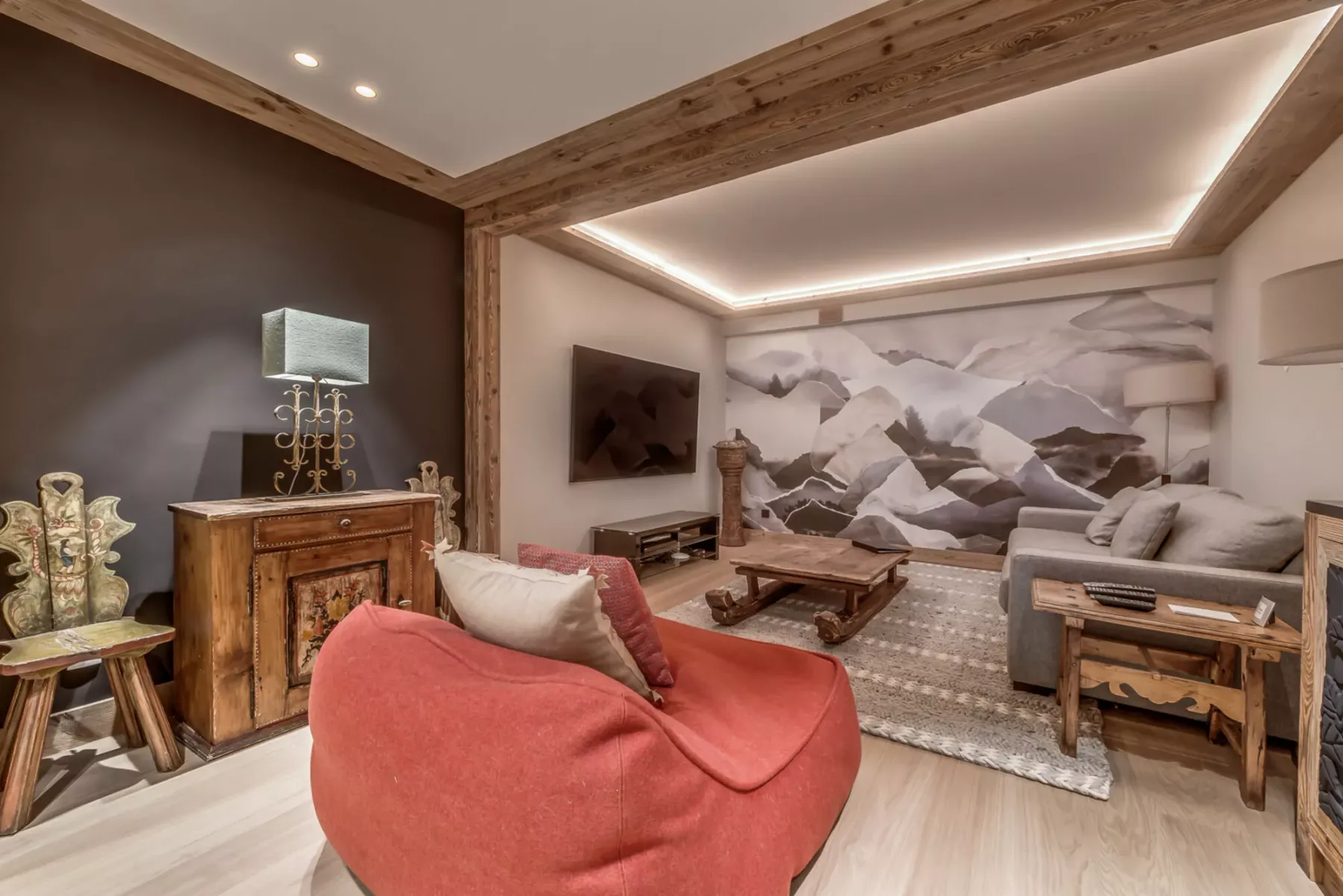 Una sala de estar con un sillón rojo, muebles de madera y un mural de montañas.
