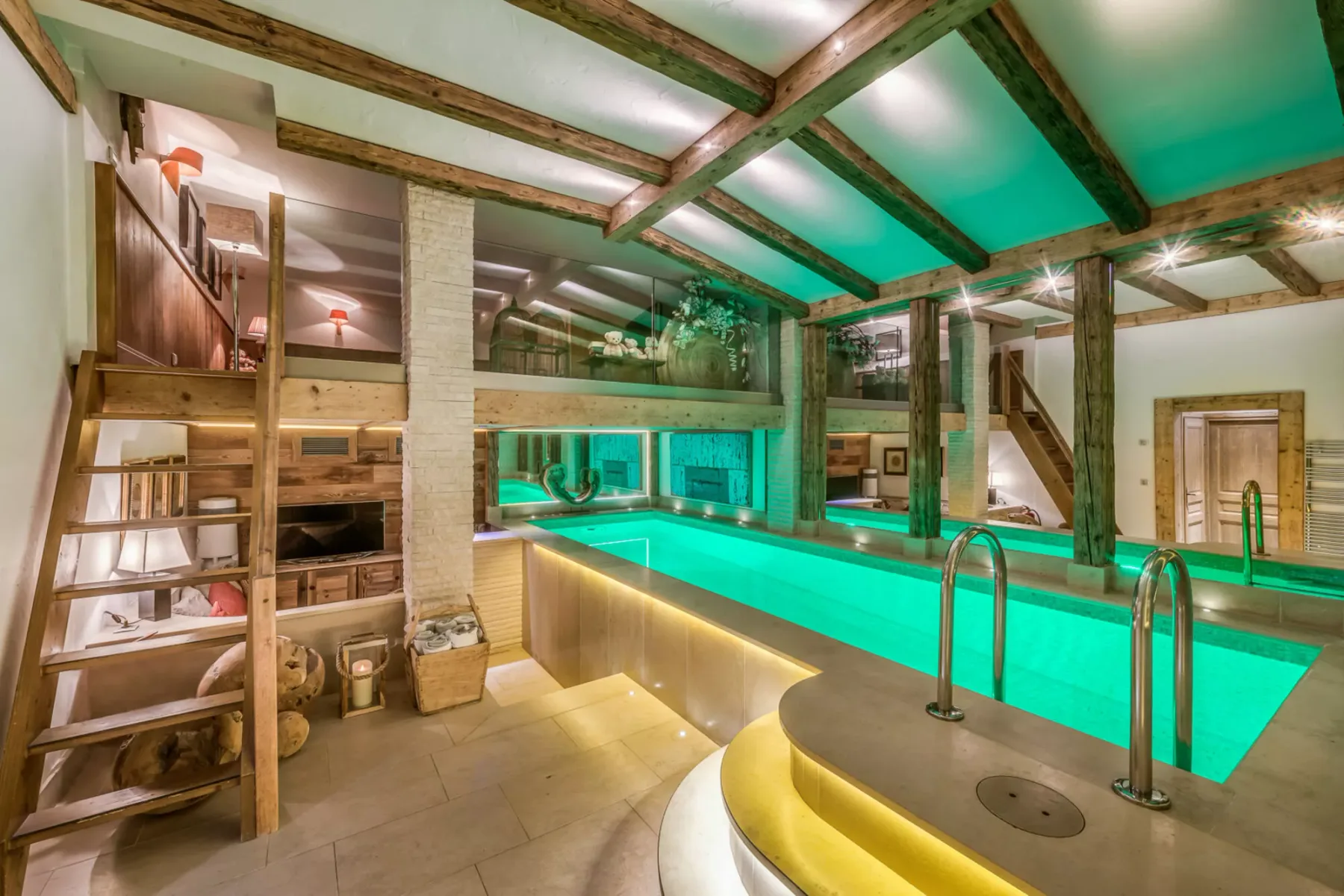 An indoor swimming pool beneath exposed wooden beams, with a ladder beside the water.