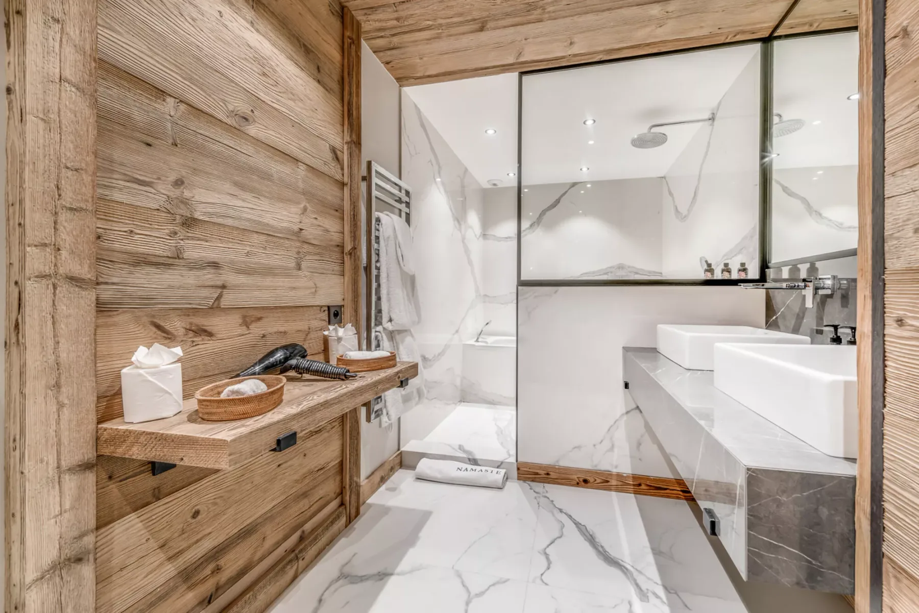 Un baño luminoso con ducha de cristal y lavabos blancos.