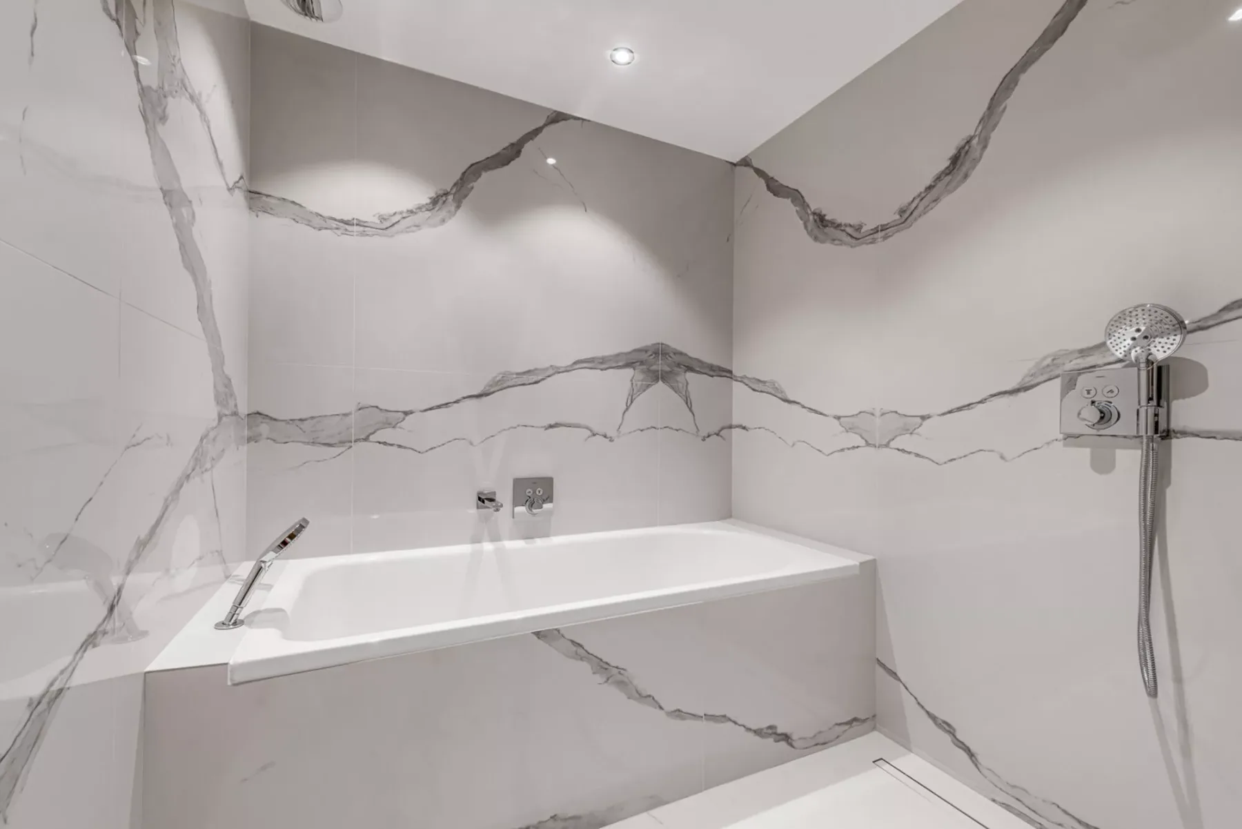 Un baño revestido de azulejos con bañera y ducha de mano en la pared.