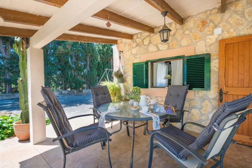 Un patio cubierto de piedra tiene asientos al aire libre alrededor de una mesa junto a una ventana.
