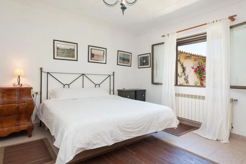 Un dormitorio con una cama blanca, cuadros enmarcados y una ventana con cortinas.
