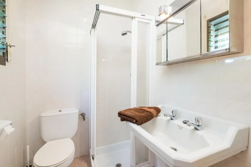 Un baño con ducha, inodoro y lavabo bajo un armario con espejo.