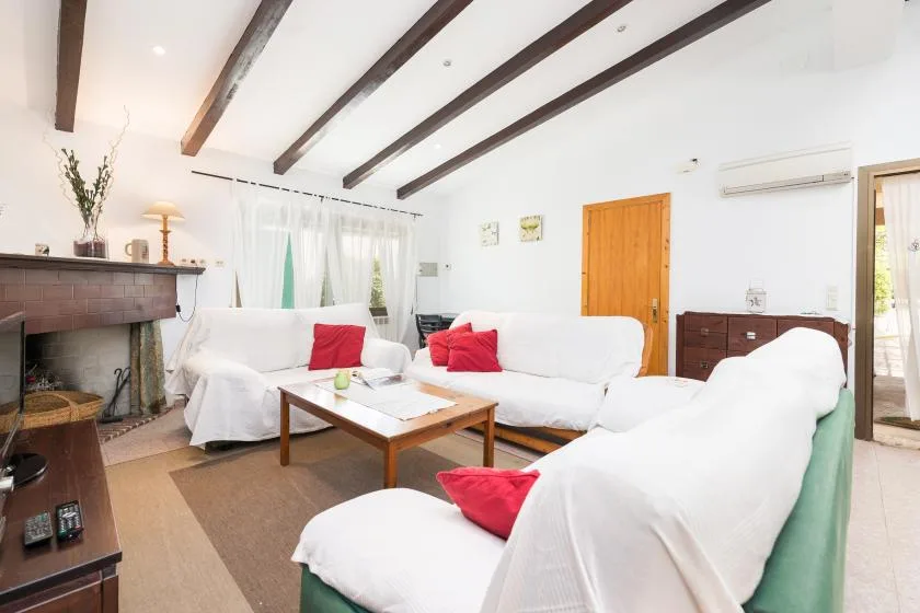 Una sala luminosa con asientos cubiertos de blanco, una mesa de centro y vigas expuestas.
