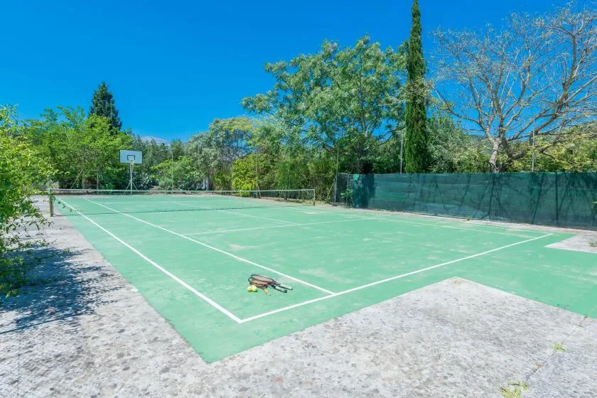 Una cancha de tenis al aire libre con una canasta de baloncesto en un extremo.