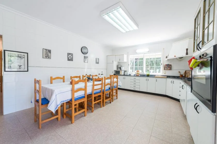 Una cocina y comedor luminosos con una mesa larga y armarios blancos.