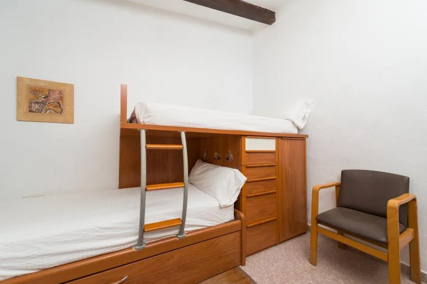 Un dormitorio con una litera de madera y una silla acolchada.