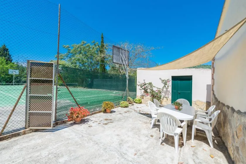 Un patio al aire libre con asientos blancos junto a una cancha cercada.