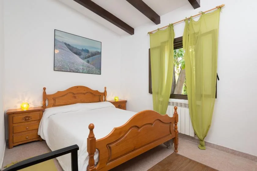 Un dormitorio con una cama de madera, mesitas de noche y cortinas verdes junto a la ventana.