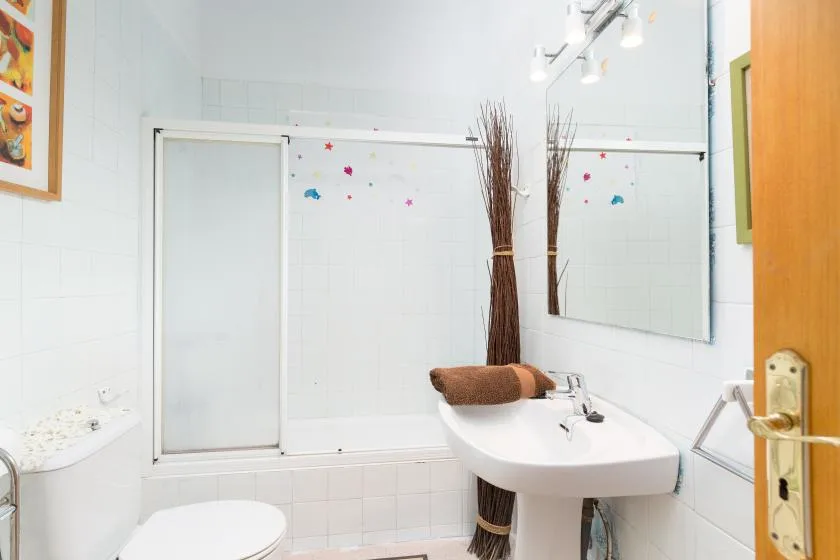 Un baño luminoso con lavabo, espejo y ducha con mampara de vidrio.