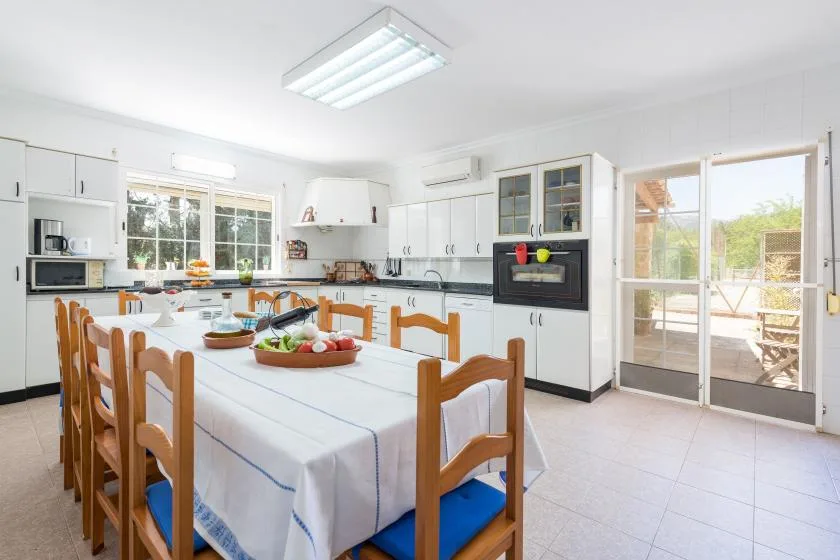 Una luminosa cocina y comedor con una mesa larga y asientos de madera.