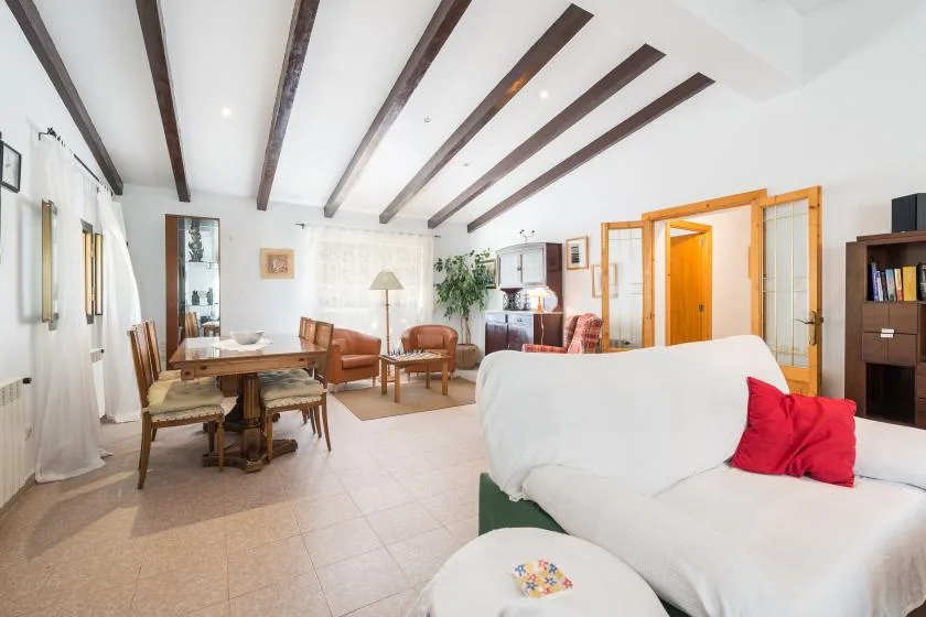 Una sala luminosa con asientos, una mesa de comedor y vigas expuestas en el techo.