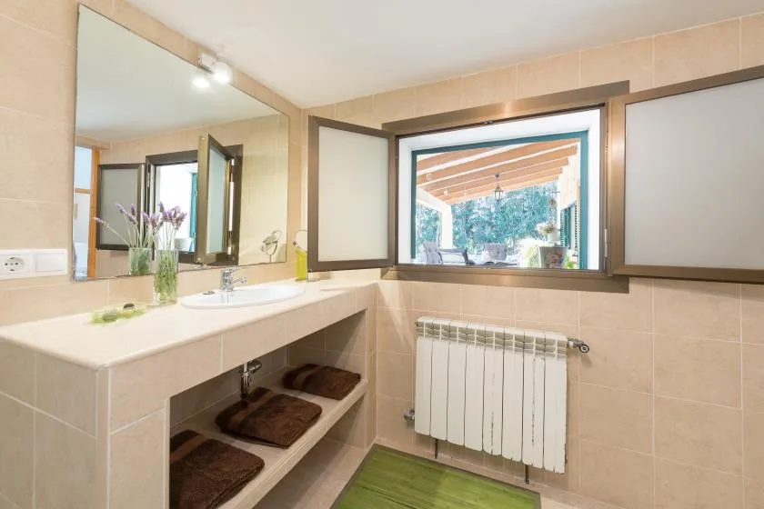 Un baño con azulejos, un tocador largo, espejo y ventana.