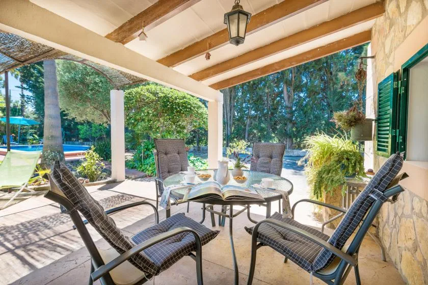 A covered patio with outdoor seating and a glass table overlooks a garden.