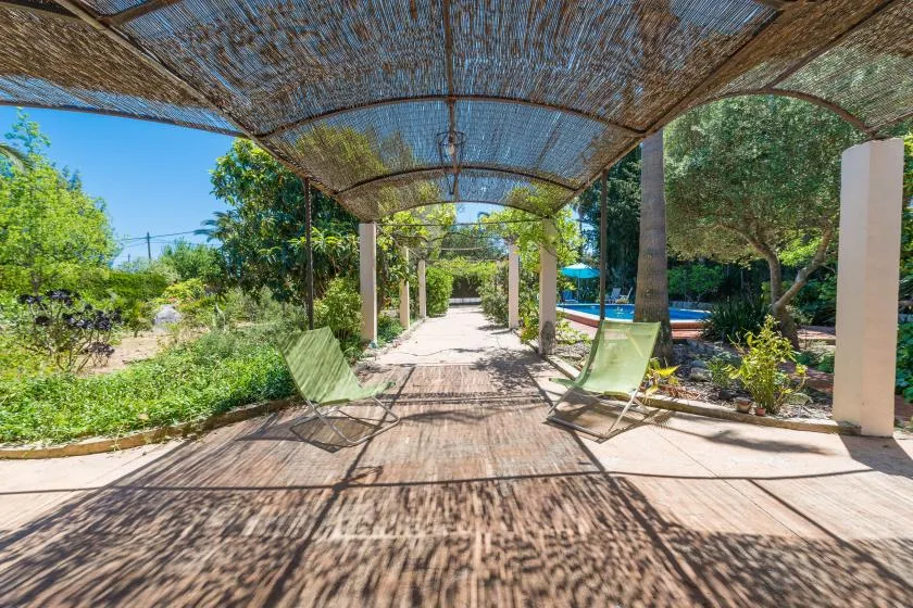 Un sendero de jardín bajo una cubierta tejida, con asientos junto a una piscina.