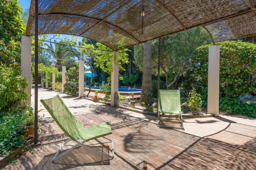 Un patio sombreado con asientos reclinables junto a una piscina.