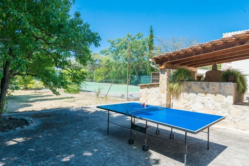 Una mesa de ping-pong al aire libre está junto a un patio de piedra sombreado.