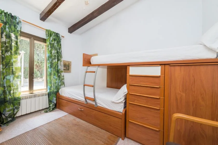 Un dormitorio con una litera de madera junto a una ventana con cortinas verdes.