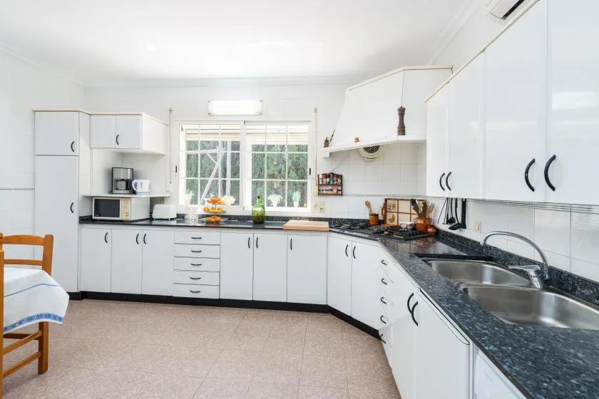 Una cocina luminosa con gabinetes blancos, encimeras oscuras y un fregadero doble.