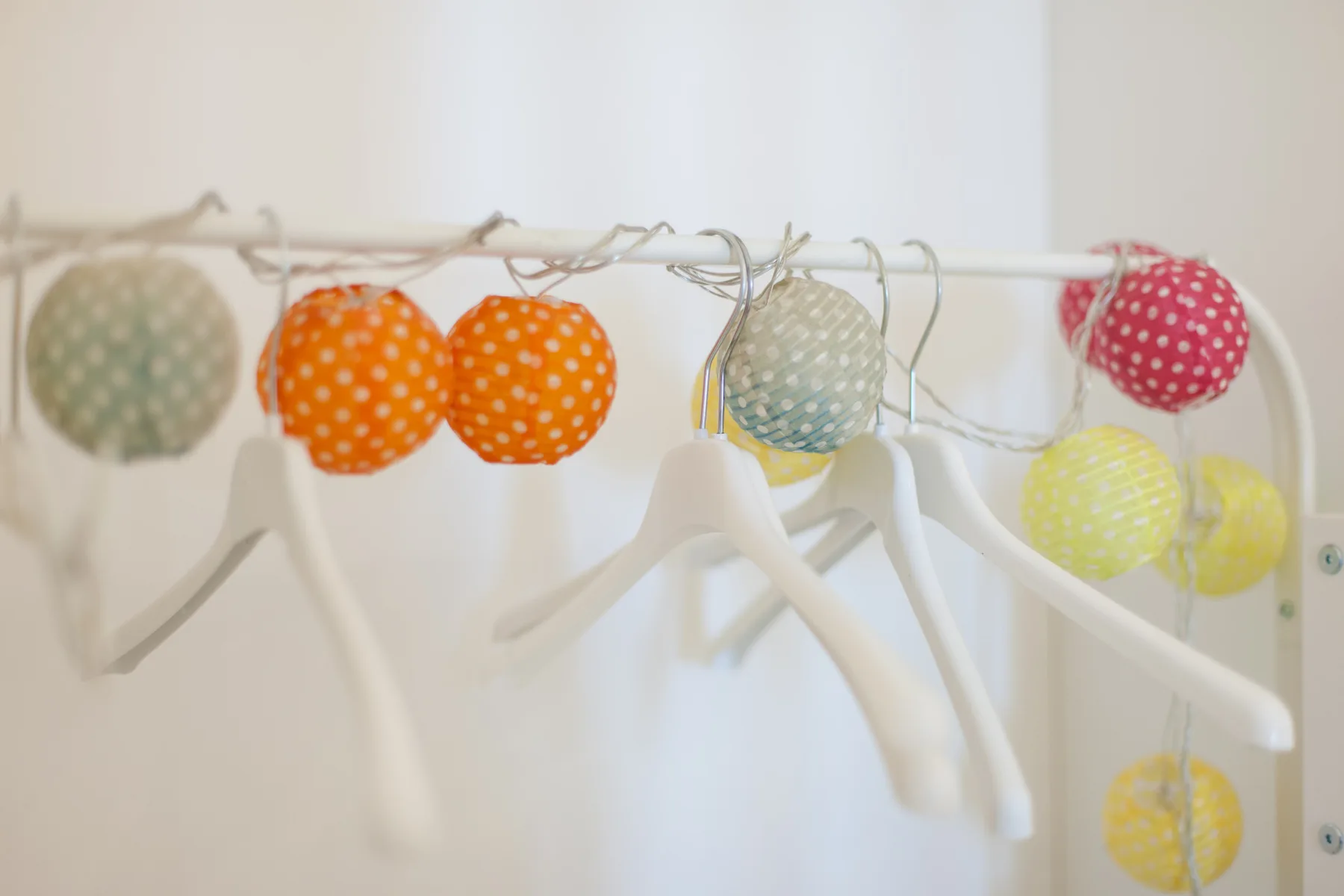 A white clothes rack holds hangers and colorful round string lights.