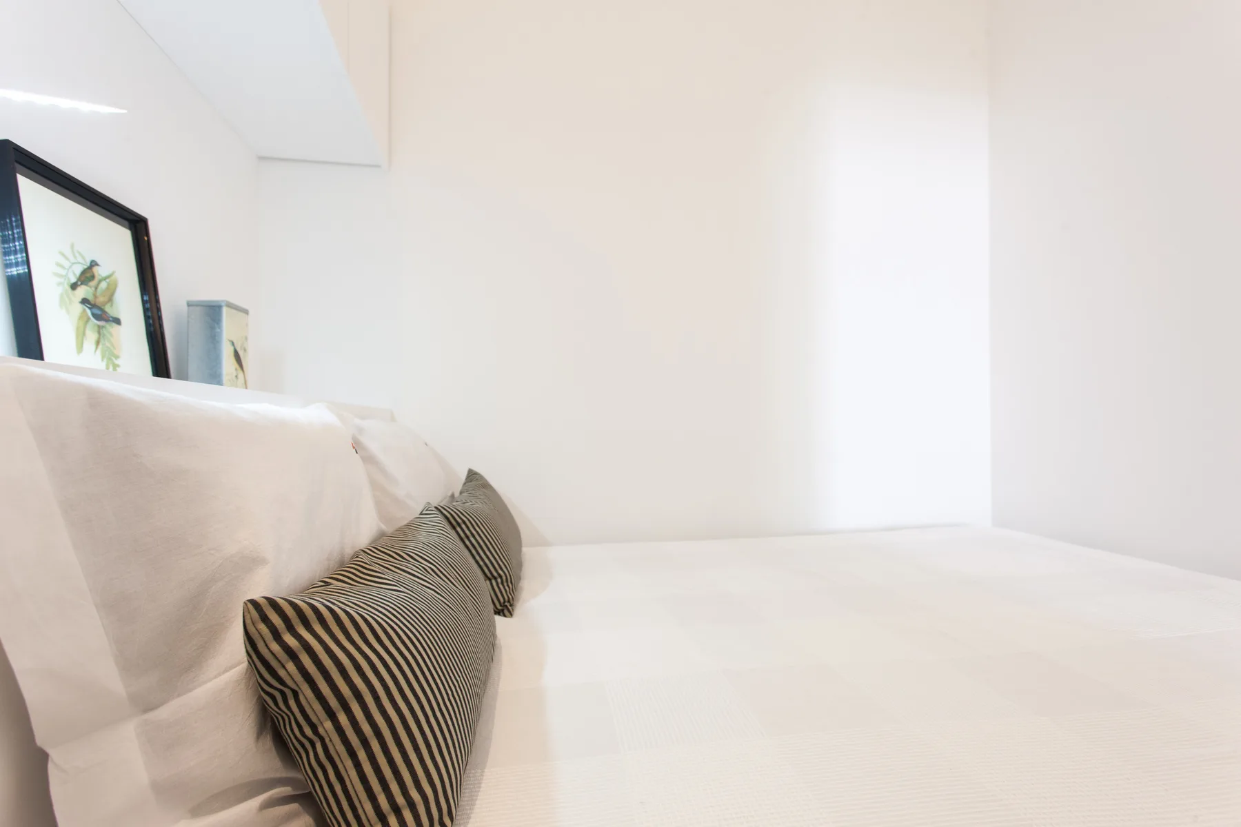 A bright bedroom with white bedding and striped accent pillows.