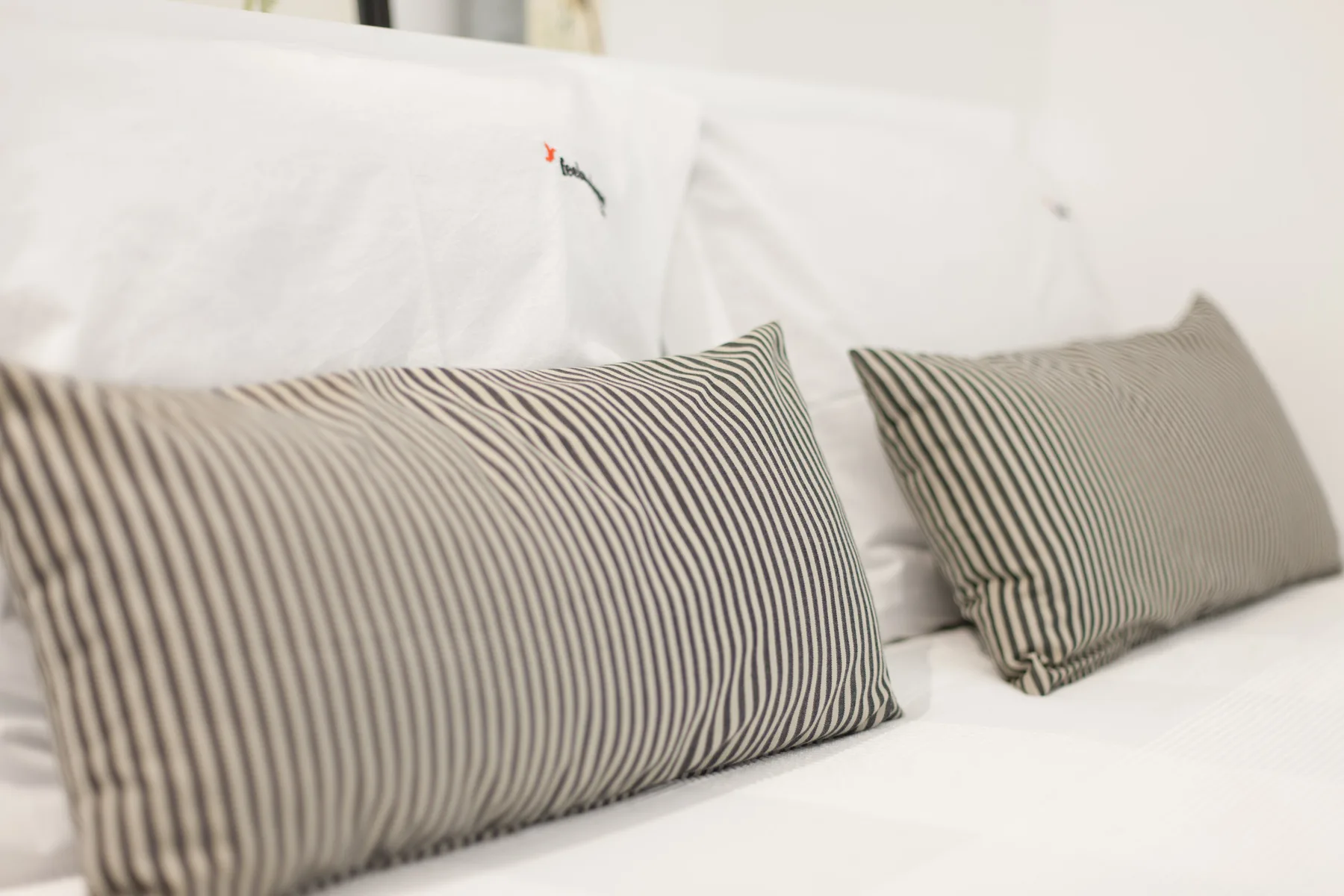 A bed with white bedding and striped accent pillows.