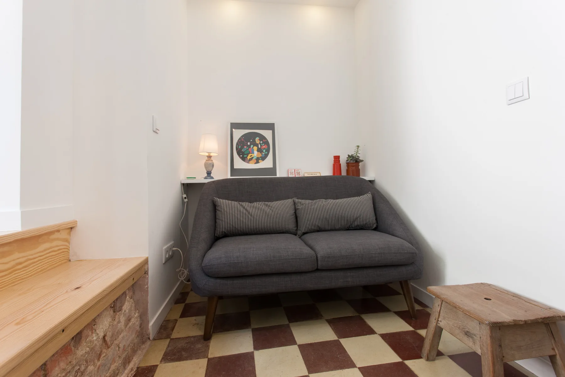 A small living area with a gray sofa, framed artwork, and checkered floor.