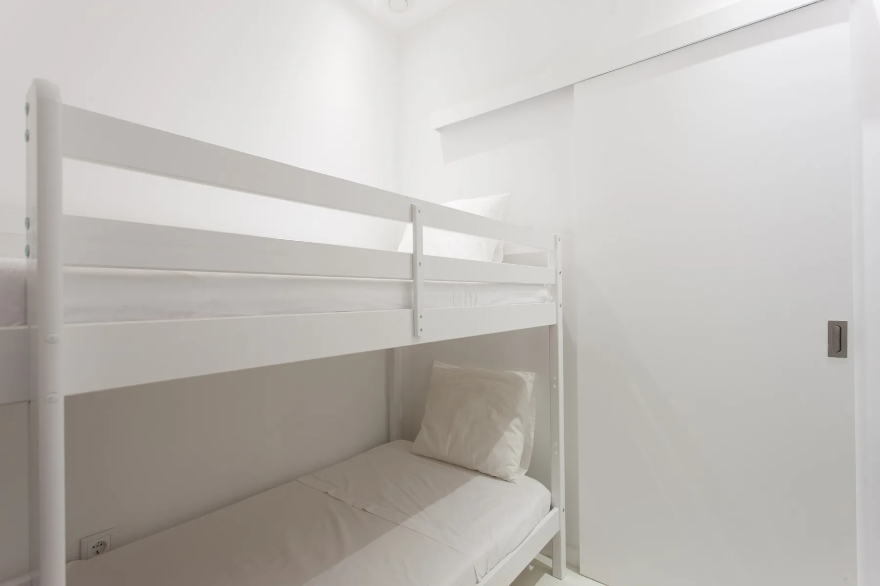 A bright bedroom with white bunk beds and a pale pillow.