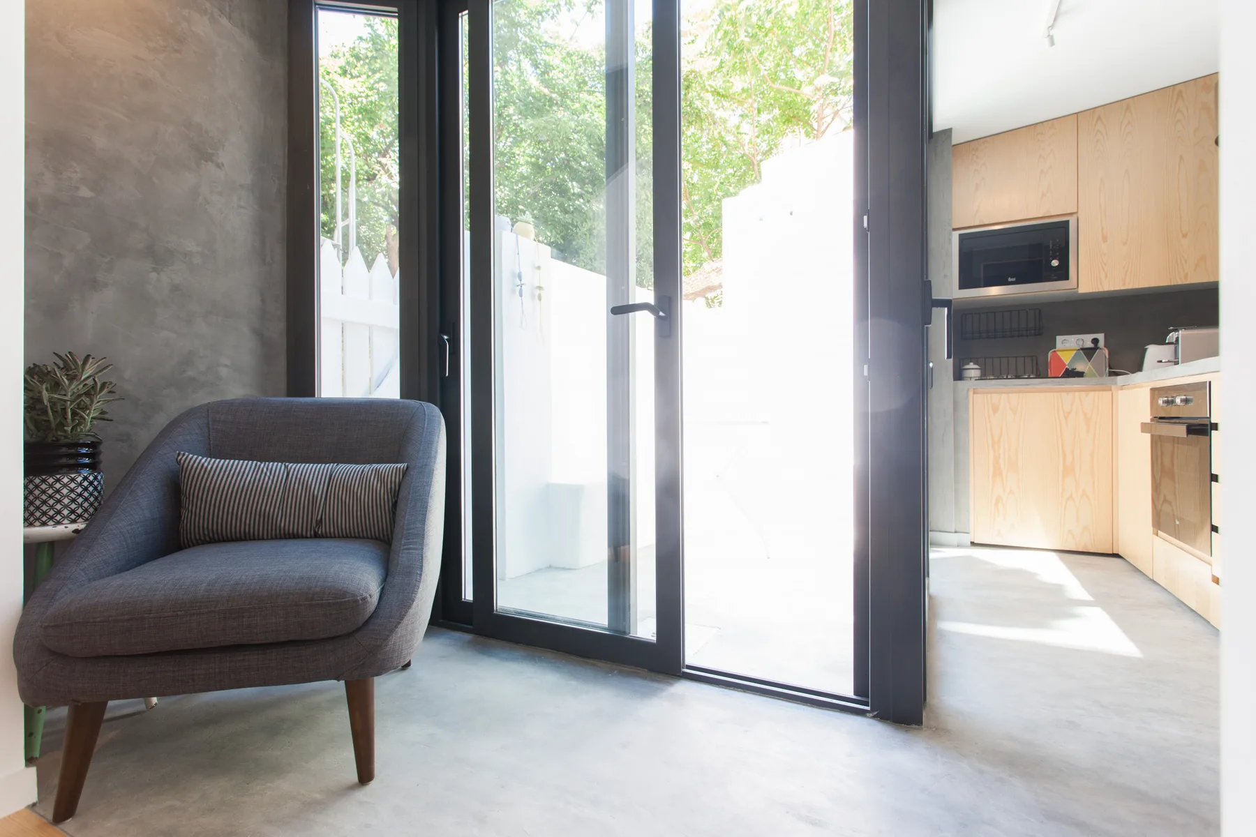A modern interior with a lounge chair beside tall glass doors and a compact kitchen.