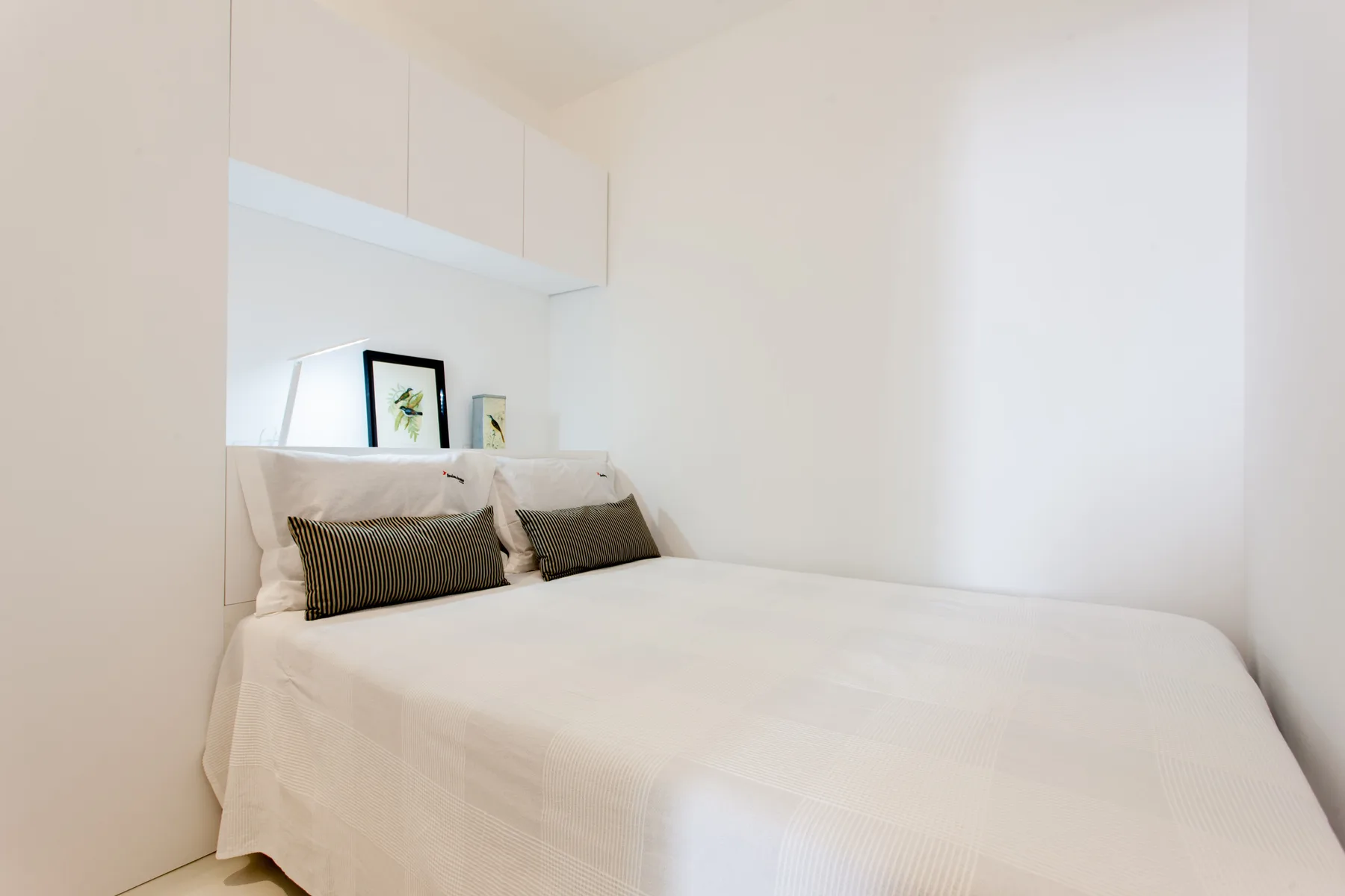 A bright bedroom with white bedding and dark accent pillows.