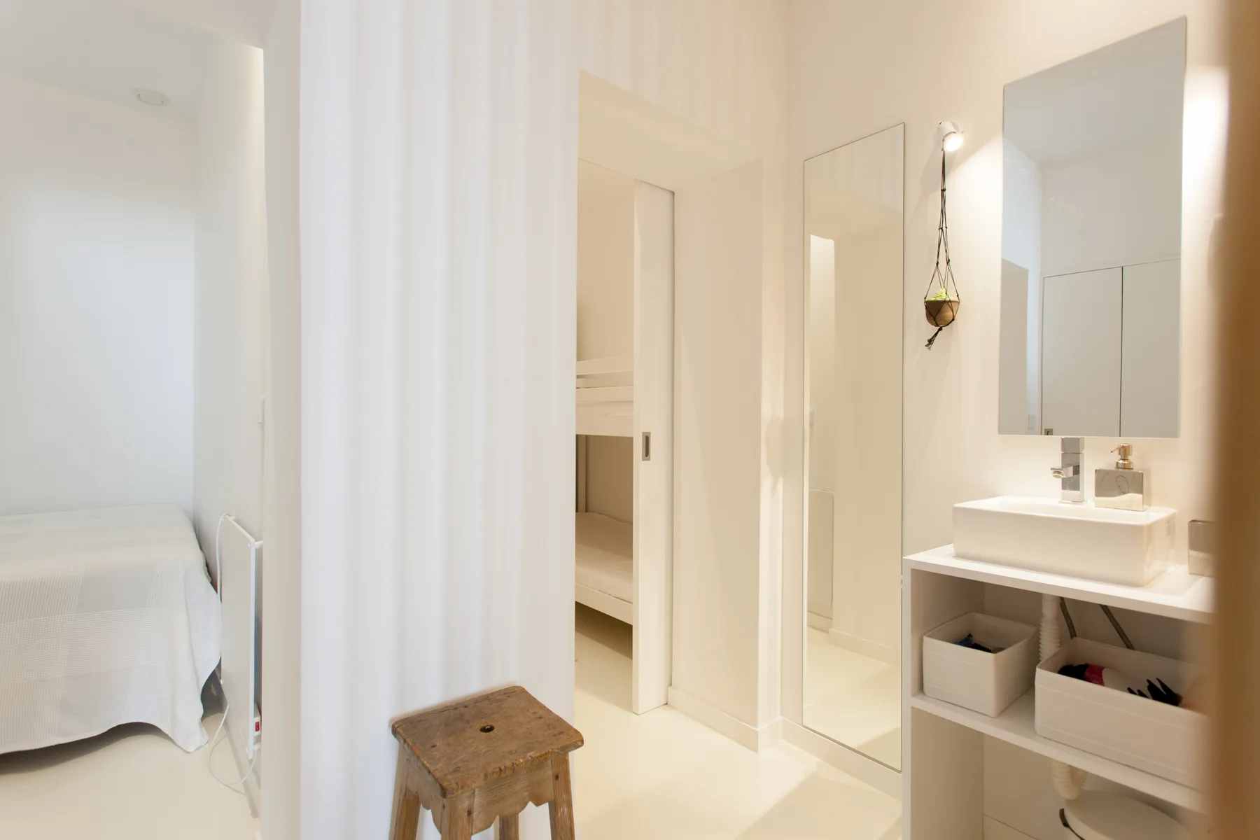 A bright bedroom area opens onto a bathroom with a sink and mirror.