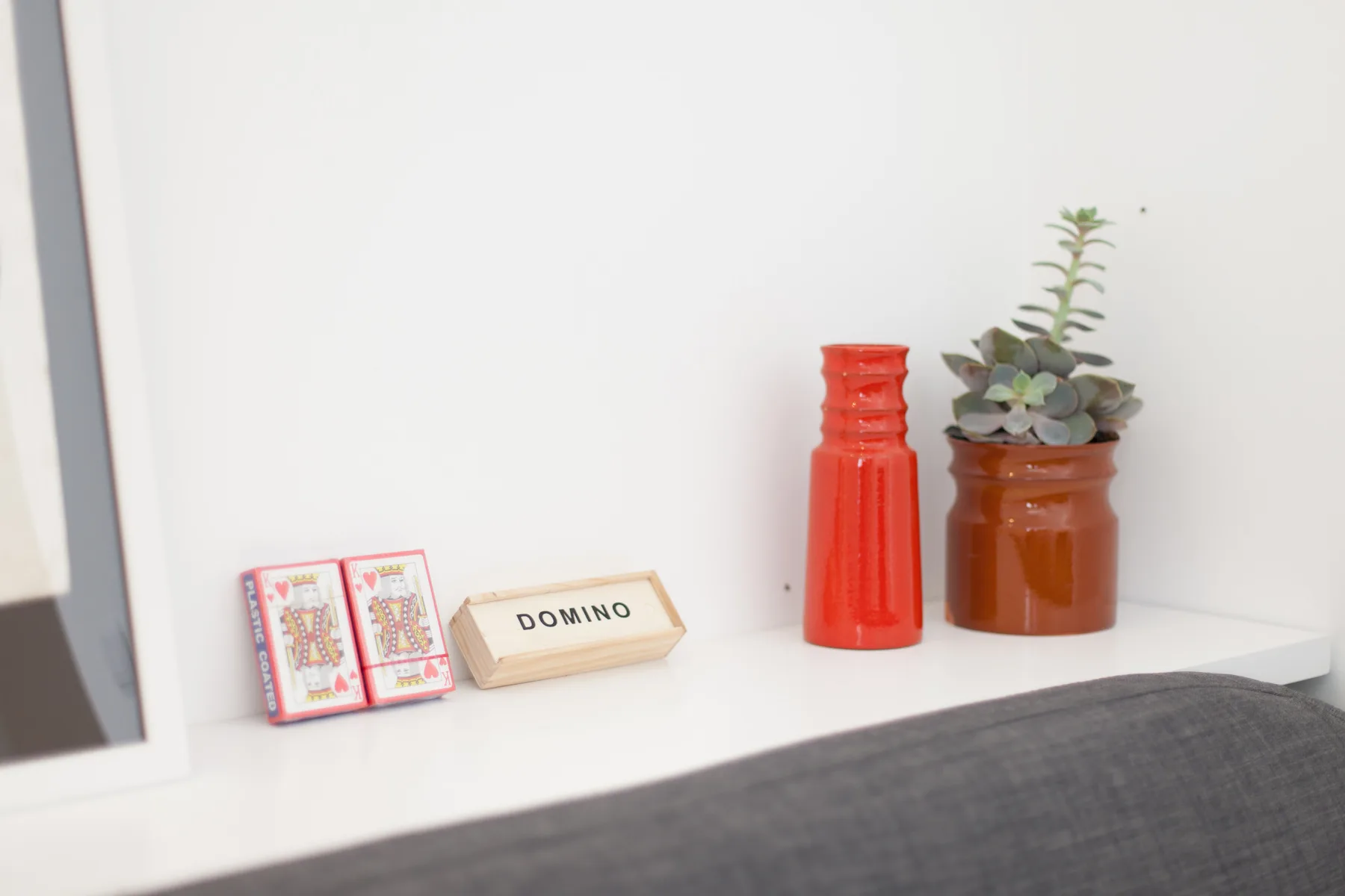 A white shelf displays a domino set, a red vase, and a potted succulent.