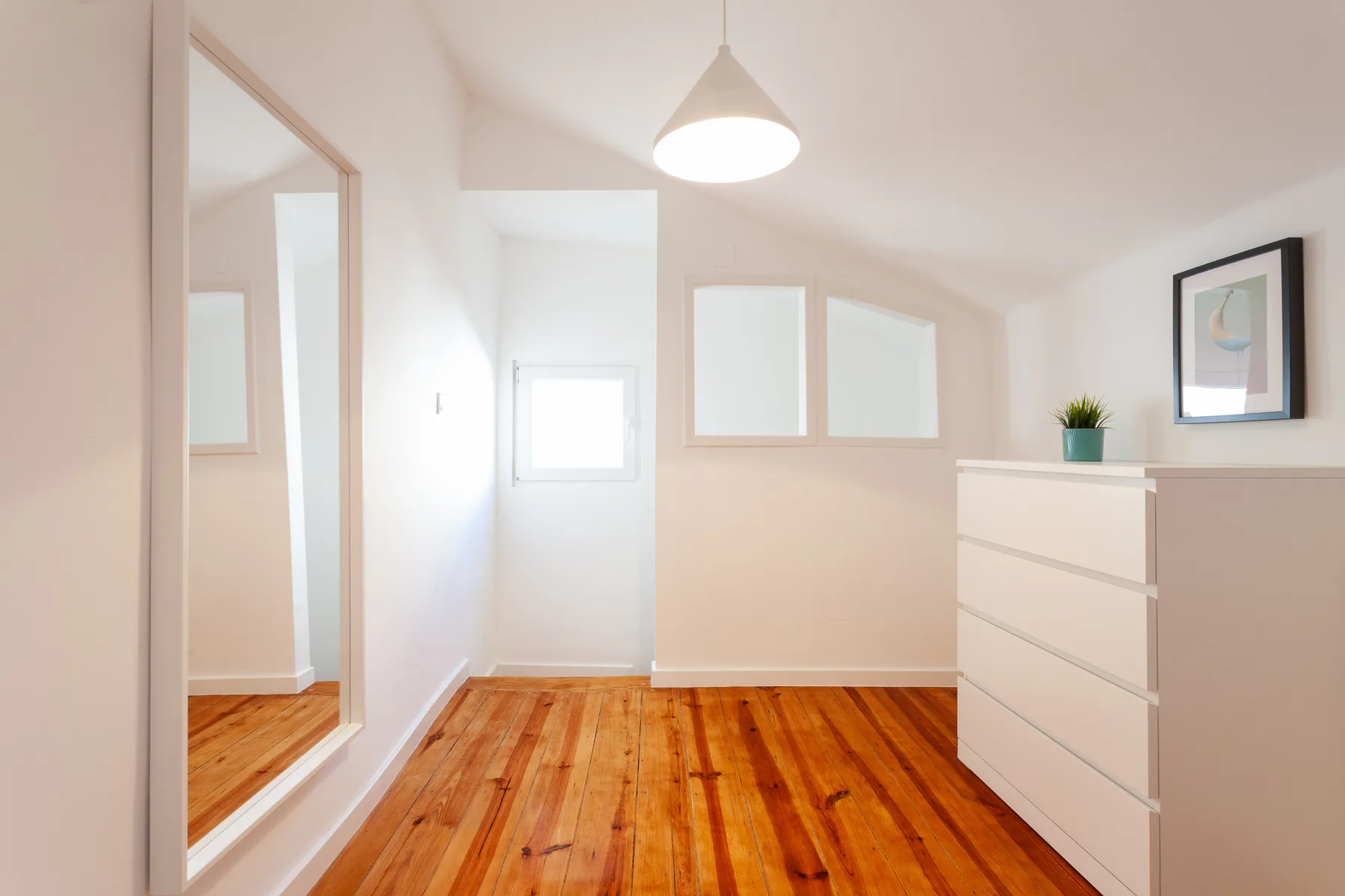 Una habitación luminosa con suelo de madera pulida y una cómoda blanca.