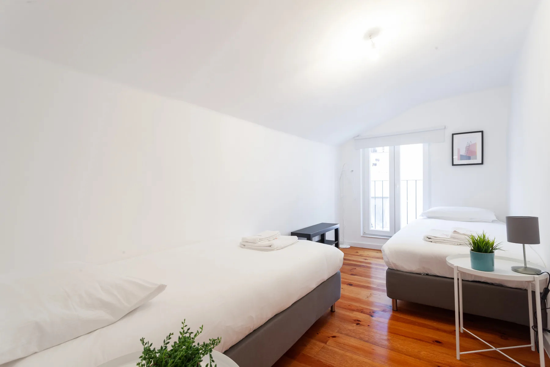 Un dormitorio luminoso con dos camas, suelo de madera y una ventana.