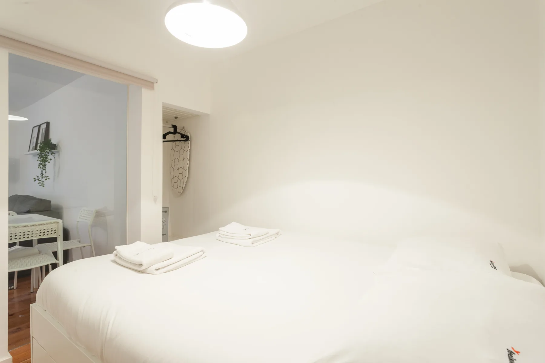 Un dormitorio con una cama bien hecha y un escritorio visible a través de la puerta.