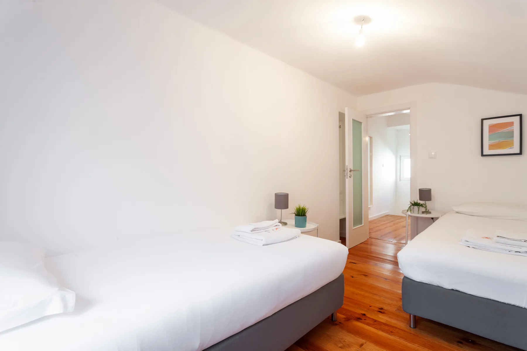 Un dormitorio luminoso con dos camas y una puerta que da a un pasillo.
