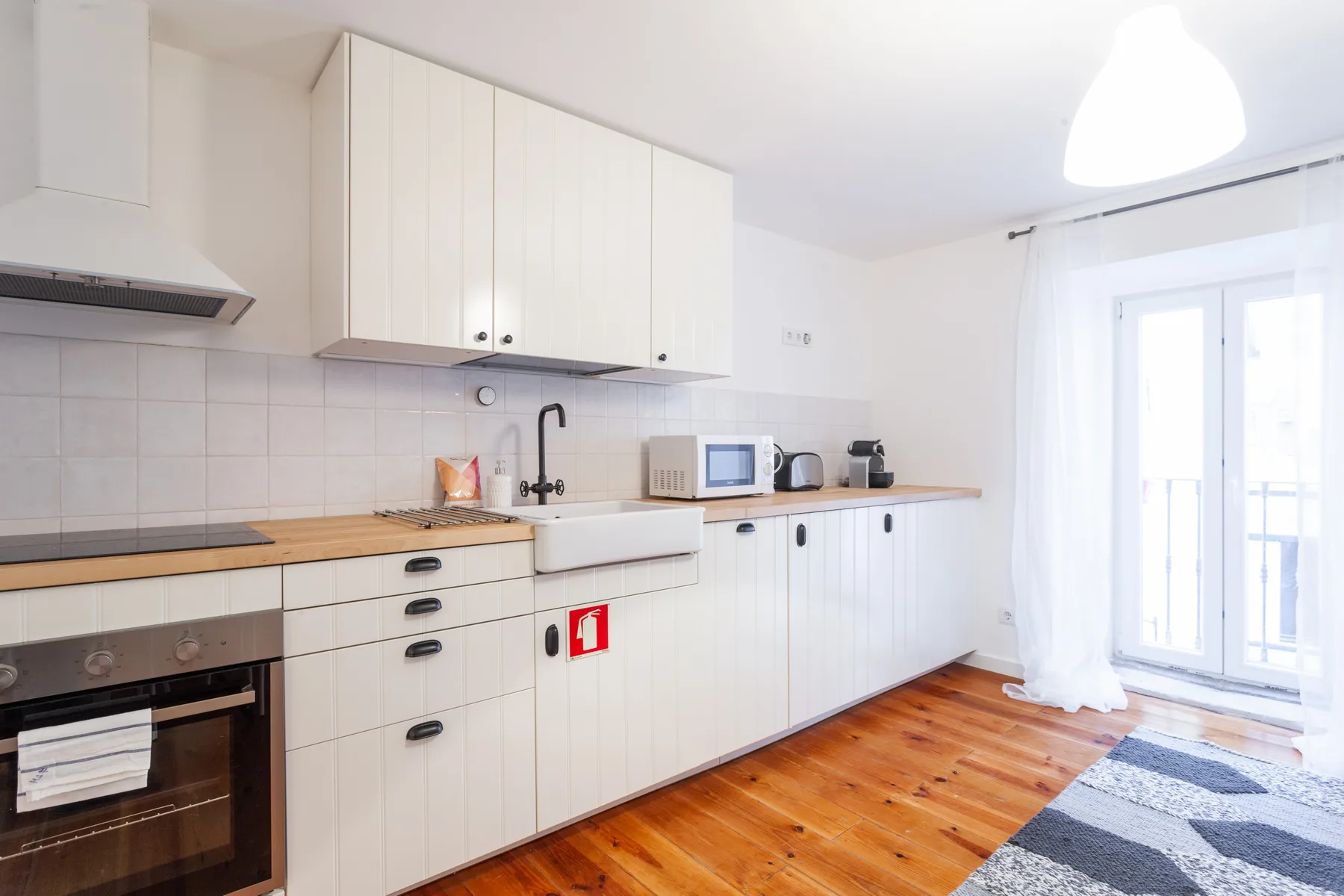 Una cocina luminosa con armarios blancos y suelo de madera.
