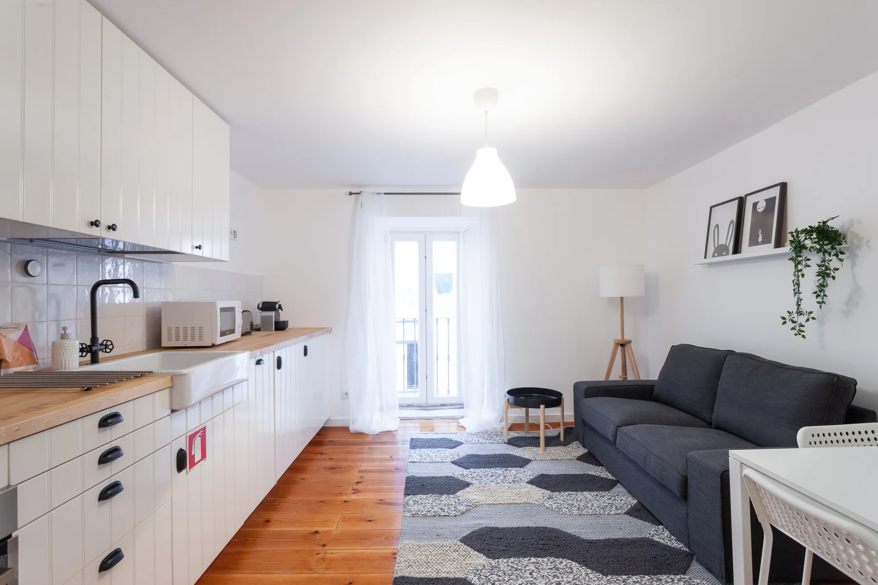 Una sala luminosa con cocina, asientos oscuros y una alfombra estampada.