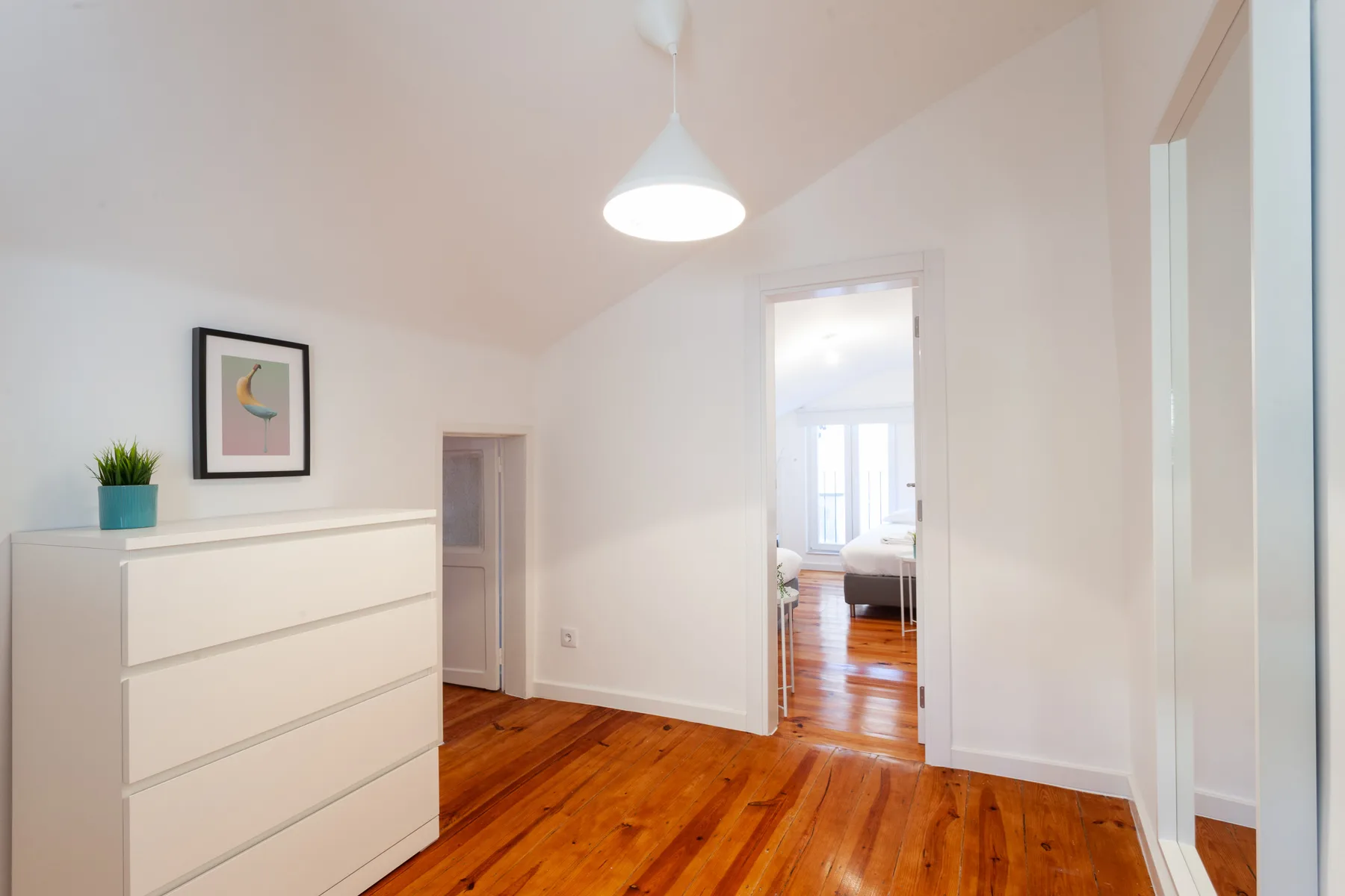 Un dormitorio luminoso con suelo de madera y una puerta que da a otra habitación.