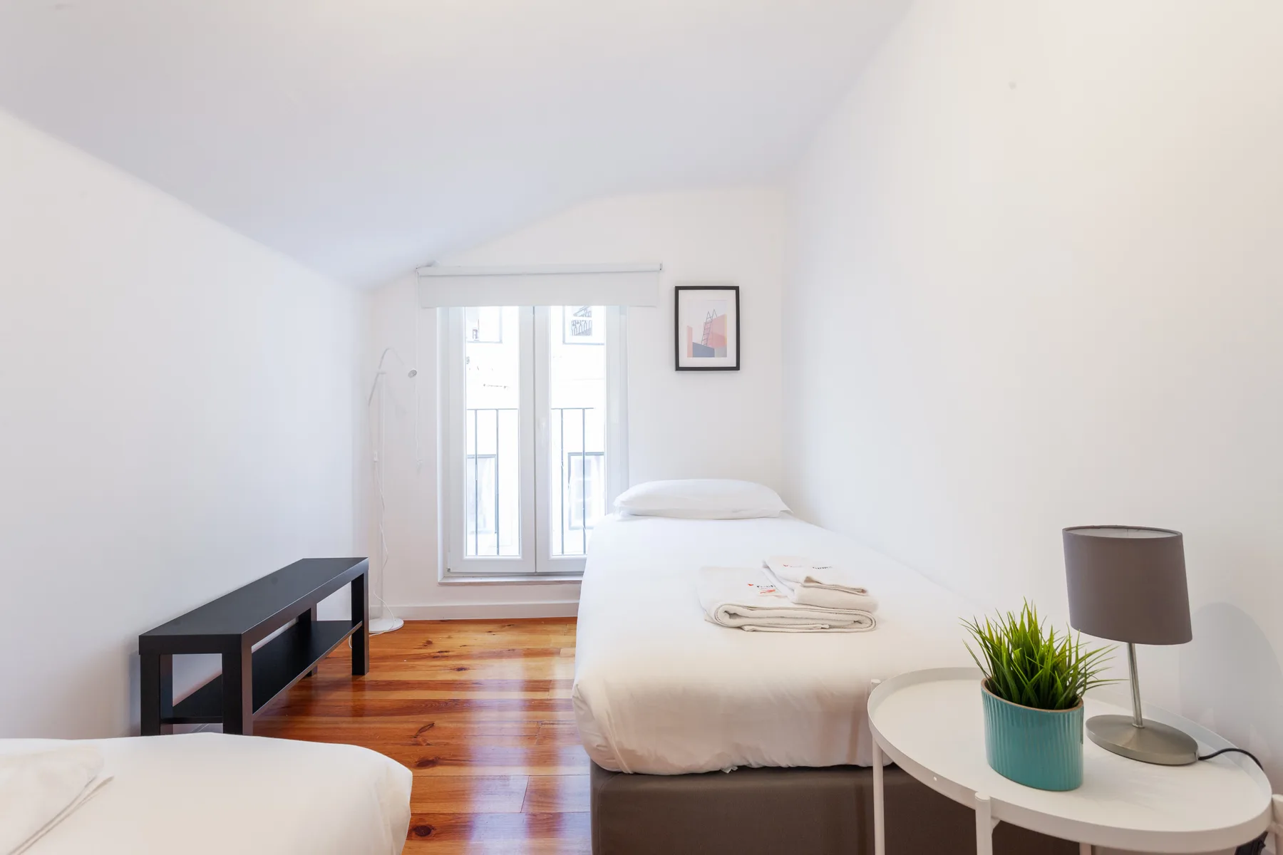Un dormitorio luminoso con una cama junto a una ventana y una mesa redonda pequeña.