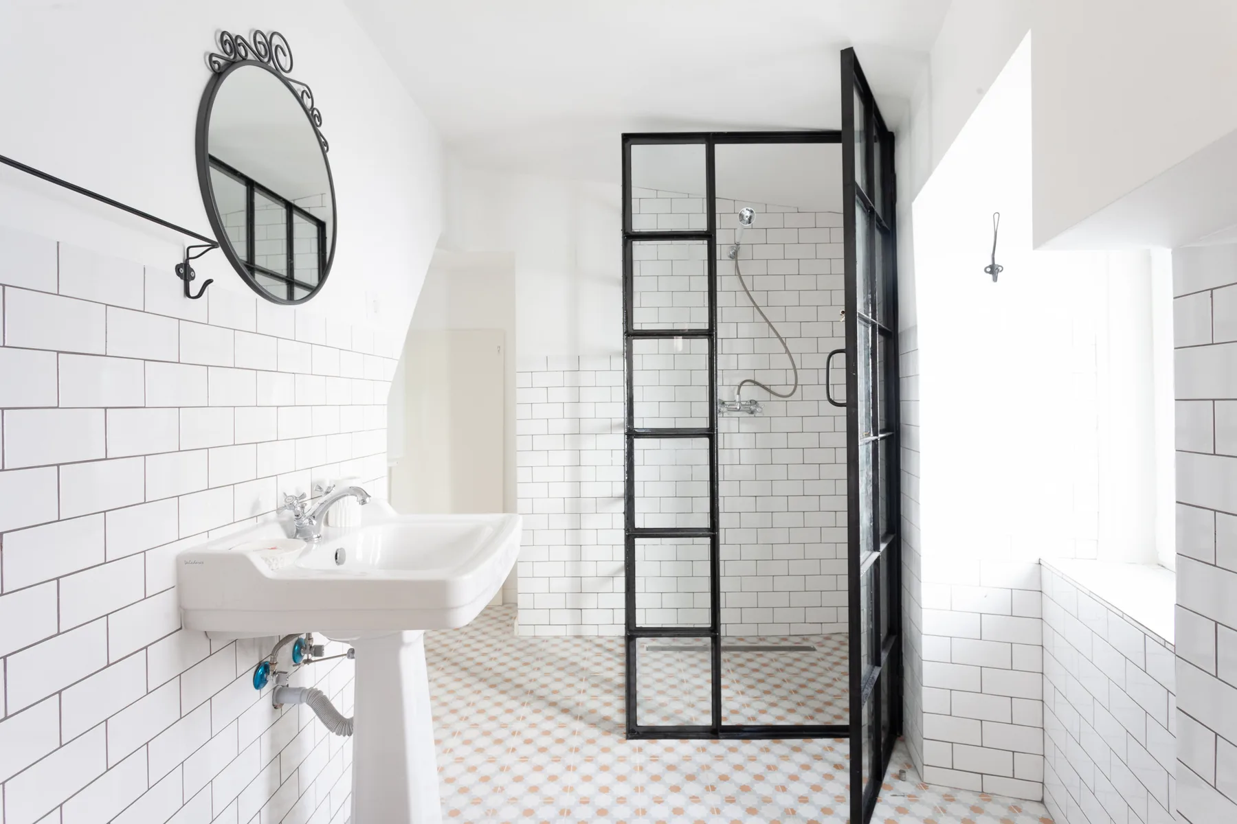 Un baño luminoso con lavabo suspendido y ducha de cristal con marco negro.