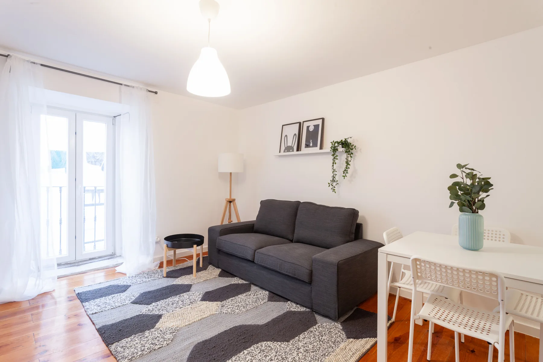 Una luminosa sala de estar y comedor con un sofá oscuro, una ventana y una mesa pequeña.
