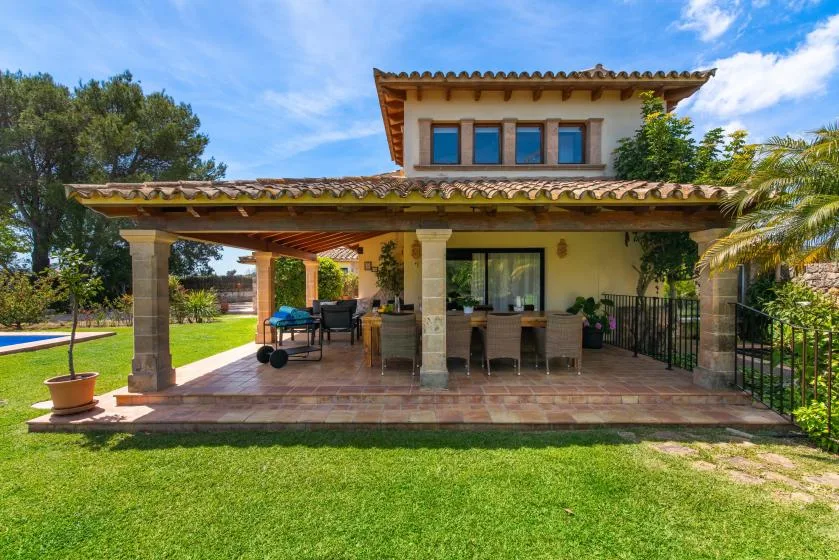 Un patio exterior cubierto con asientos de comedor da a un césped verde y una piscina.