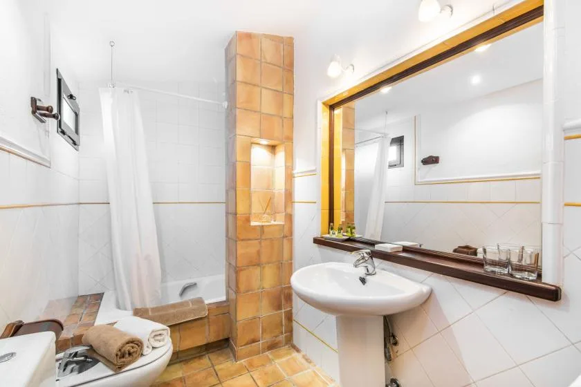Un baño con azulejos, lavabo, espejo grande y una zona de ducha con cortina.