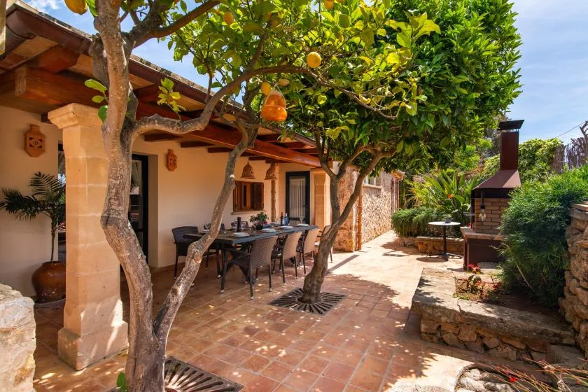 Un patio de comedor a la sombra, con árboles, una mesa y vegetación alrededor.
