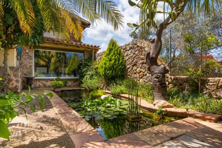 Un estanque de jardín con nenúfares está junto a un sendero de piedra y un edificio.
